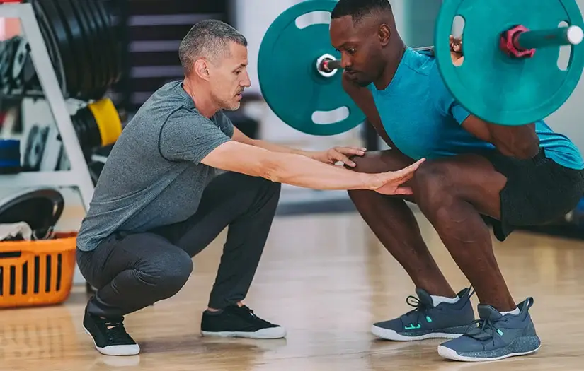 A coach correcting an athlete’s form while they perform a squat